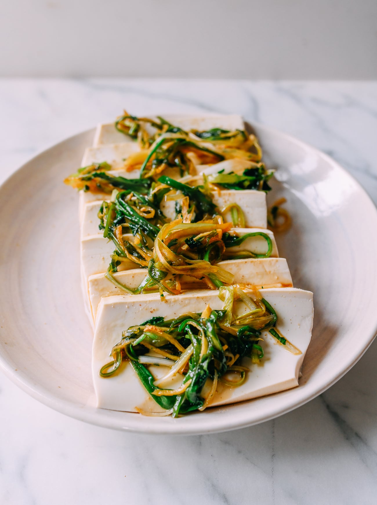Spreading cooked scallions, cilantro, and ginger on top of tofu