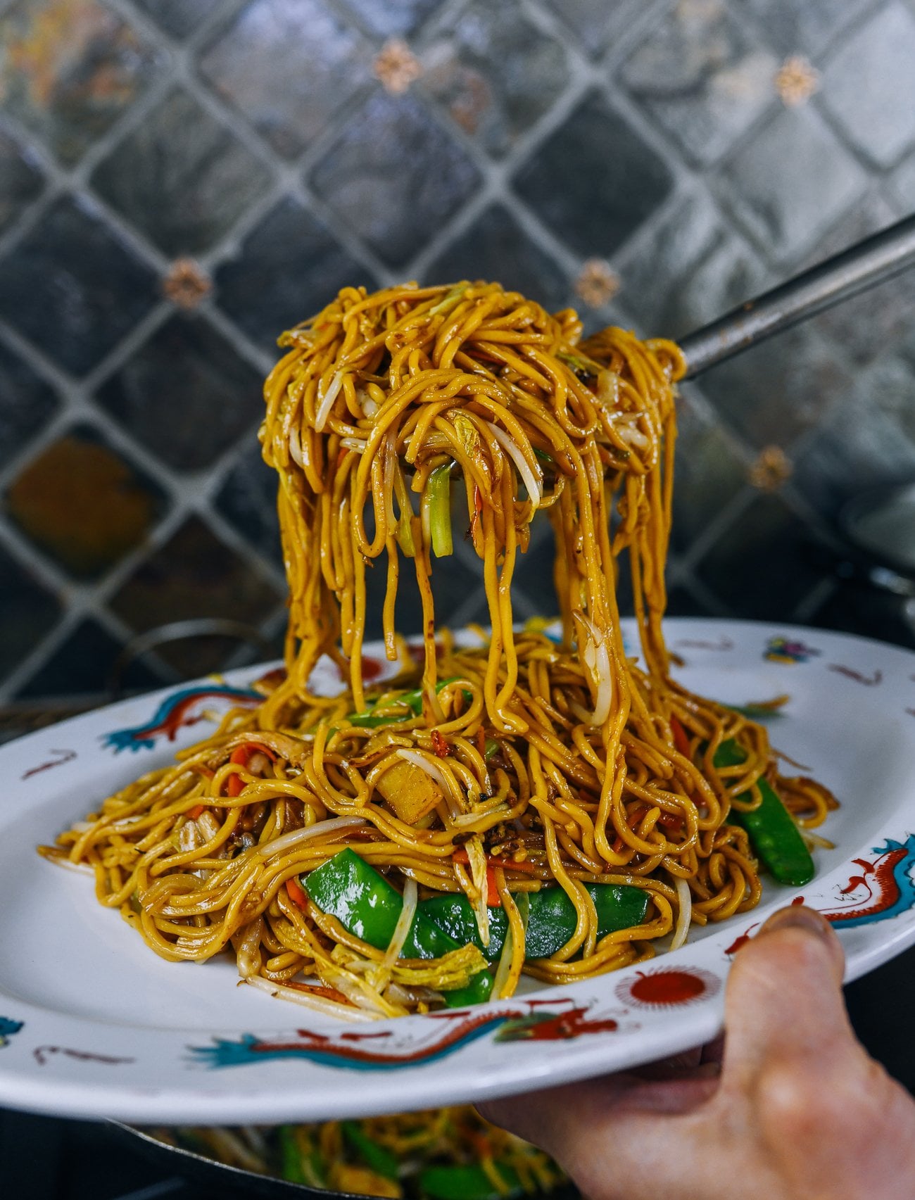 Lifting lo mein out of wok and transferring to serving platter
