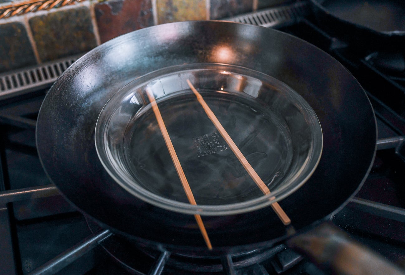 plate balanced on chopsticks in wok for steaming