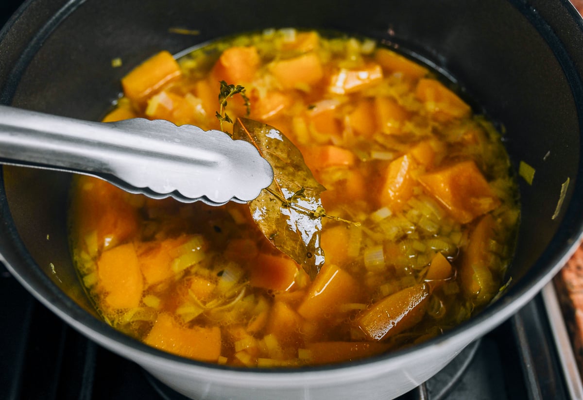 removing bay leaves and thyme from pot of simmered pumpkin